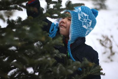 Boy reaching for pine tree with snow in background