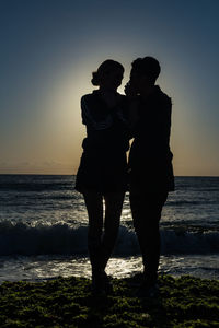 Couple standing on beach against sky during sunset