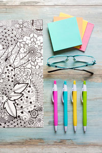 Close-up of pens with colorful paper and eyeglasses on table