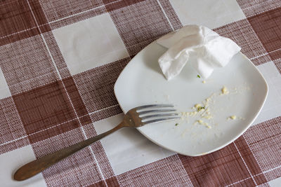 Empty white dish with leftovers of eaten food, crumpled table-napkin and steel fork