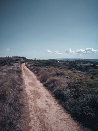 Dirt road amidst field against sky