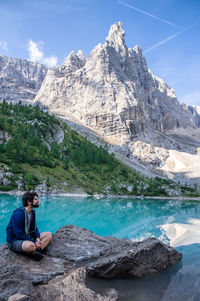 Man sitting on rock by lake against sky