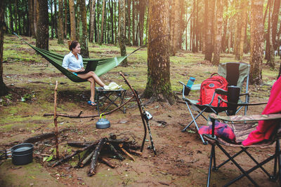 Woman using laptop while sitting on hammock in forest