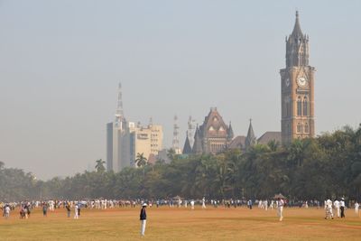 Playing cricket at oval maidan with clock tower behind at mumbai