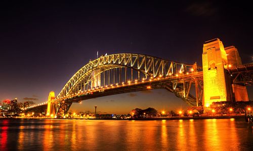 Illuminated bridge over river against sky in city at night