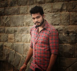 Portrait of young man standing against stone wall