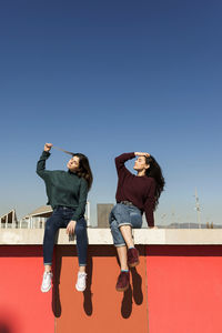 Women sitting on retaining wall during sunny day