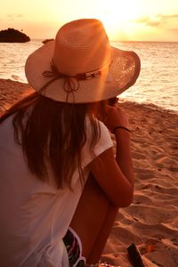 Rear view of woman wearing hat at beach during sunset