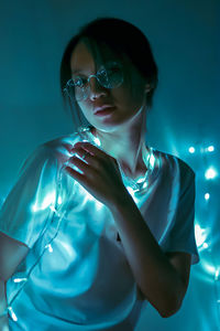 Young woman with illuminated string lights standing at home