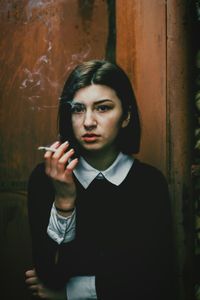 Young woman smoking against rusty wall