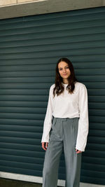 Portrait of beautiful young woman standing against wall