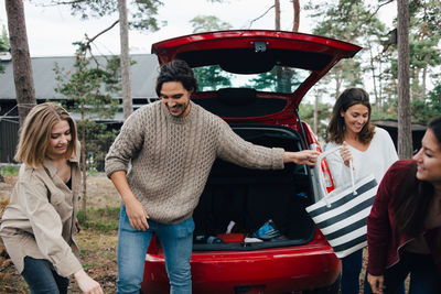 Male and female friends unloading luggage from car in back yard