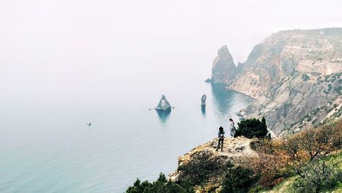 High angle view of people standing on rock formation by sea during foggy weather