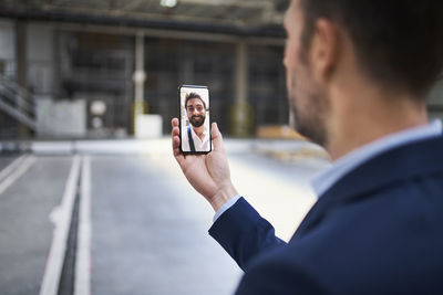 Close-up of businessman using smartphone chatting with colleague in factory