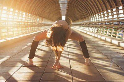 Full length of female athlete exercising on footbridge during sunset