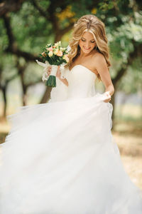 Smiling bride with bouquet spinning in white dress