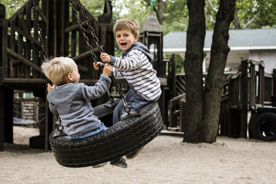 Happy brothers enjoying on tire swing in playground