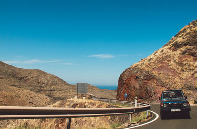 Road by rocky mountains against clear blue sky