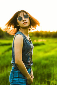 Portrait of woman in sunglasses standing on field against sky
