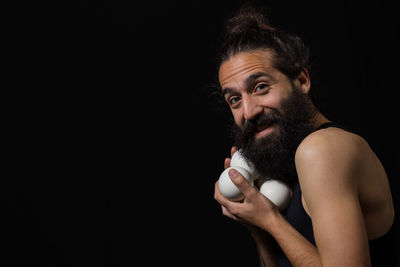 Portrait of bearded man with balls while standing against black background