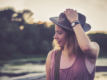 Smiling young woman looking away while standing against sky during sunset