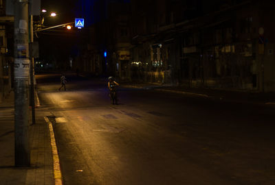Man walking on illuminated street amidst buildings at night