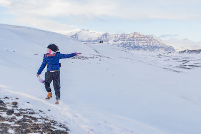 Rear view of woman with arms outstretched walking on snow covered land