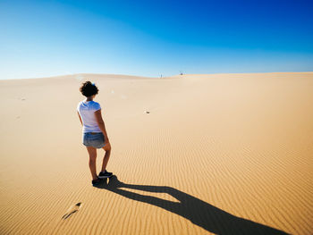 Rear view of woman standing on sand dune