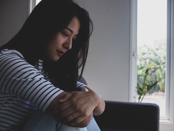 Woman looking away while sitting on window at home