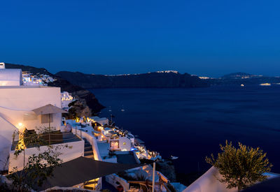 High angle view of illuminated buildings by sea against blue sky