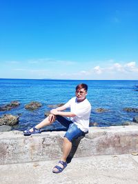 Man sitting on retaining wall by sea against sky