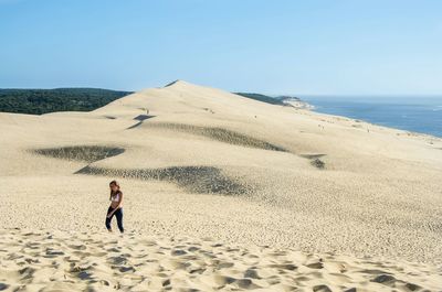 Woman walking at sandy beach against clear blue sky