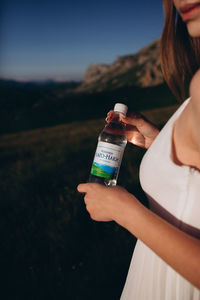 Midsection of woman holding bottle while standing on field against sky