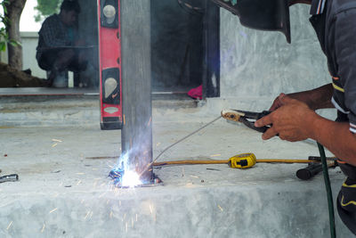 Welder with face shield is welding the steel column with the plate on the concrete floor