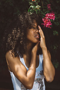 Thoughtful young woman with curly hair standing against plants