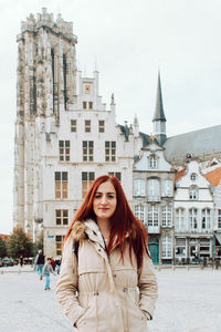 Portrait of smiling young woman standing against building in city