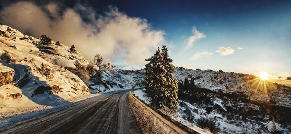 Panoramic view of road amidst snowcapped mountains against sky during winter