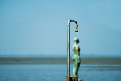 Metallic shower and statue at beach against sky