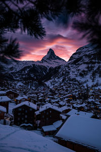 Snow covered houses and mountains against sky during sunset