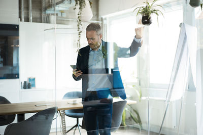 Businessman using tablet computer in meeting room seen through glass wall