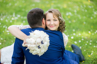 Woman embracing man while sitting on field at park