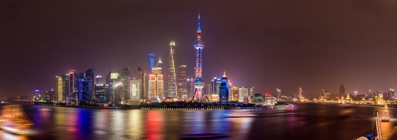 Oriental pearl tower by river against sky in city at night