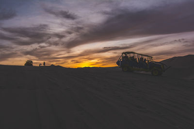 Tourists in dune buggy on sand at dusk