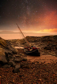 Sailboats moored on beach against sky at night