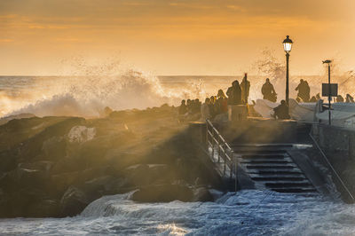 People on the rocks at sunset during a stormy sea