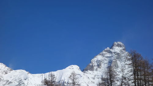 Low angle view of snowcapped mountains against clear blue sky