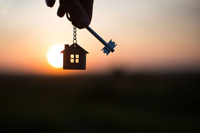 Silhouette of a house figure with a key, a pen with a keychain on the background of the sunset. 