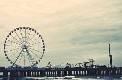 Ferris wheel by pier against sky at sunset