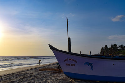 Boat moored on beach against sky during sunset