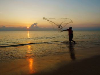 Silhouette man standing on beach against sky during sunset